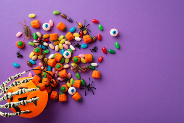 万圣节的概念。俯视图照片的骨骼手拿南瓜篮子与糖果眼睛蟑螂蜈蚣和蜘蛛在孤立的紫色背景图片下载