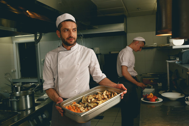 厨师站在餐厅的厨房里，端着烤蔬菜托盘图片下载