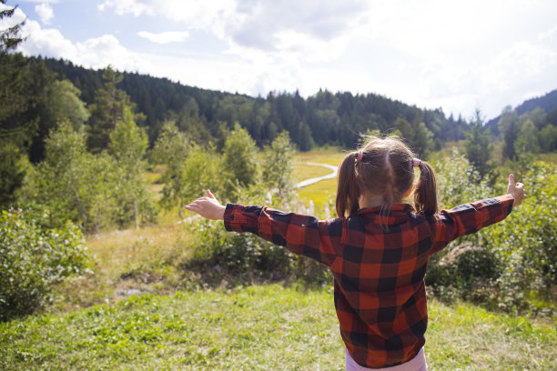童女，后视图，张开双臂在一个阳光明媚的日子里欣赏自然山景。意大利，Pian di genembro。图片下载