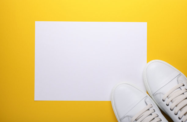 白色皮革运动鞋与一张白色的纸在黄色的背景。从以上观点。图片下载