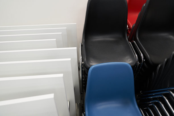 黑色和蓝色的塑料椅子堆叠在折叠的铁架子旁边。许多塑料椅子靠在墙壁的背景上，一排一排地立着。图片下载