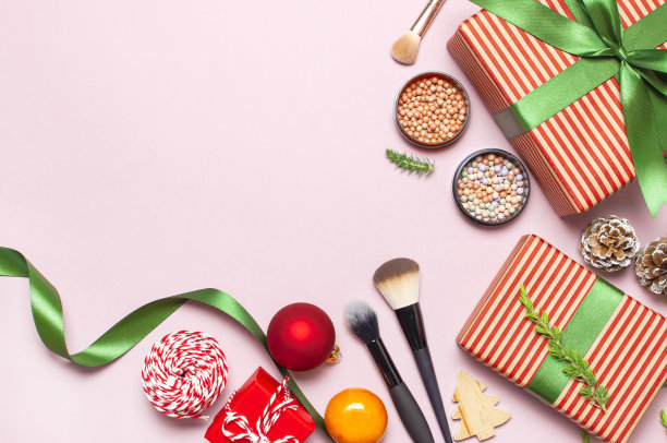 各种彩妆产品，腮红，粉饼，刷子，口红，眼影和圣诞礼物，冷杉树枝，红球在粉红色的背景平铺俯瞰新年概念，冬季装饰图片下载