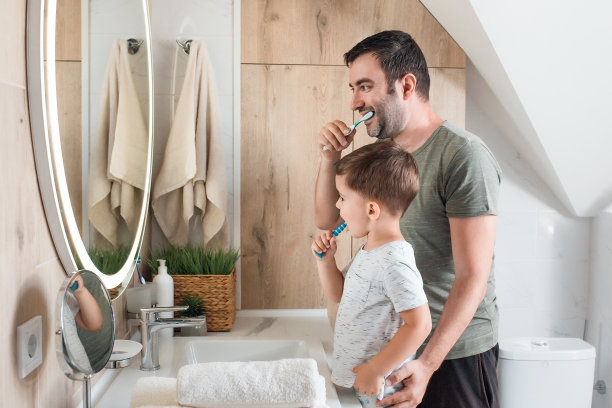 肖像微笑的父亲和快乐的小儿子在t恤拿着牙刷附近的镜子图片下载