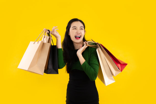 年轻的亚洲女子长头发在绿色和黑色的连衣裙携带纸袋摆在黄色的背景。图片下载