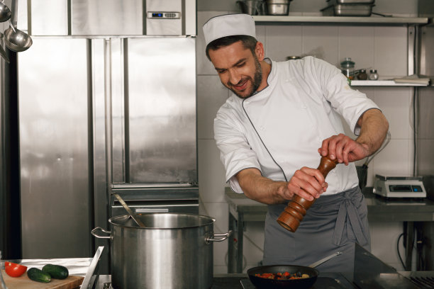 厨师在餐厅厨房烹饪时往菜里加盐或胡椒粉图片下载