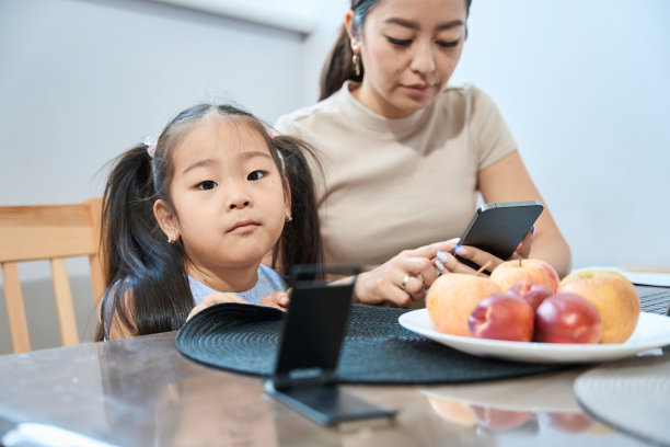 有工作的妈妈和无聊的女儿坐在桌子旁摆弄小玩意图片下载