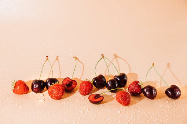 一个大的樱桃和草莓与水滴接近在阳光下的浅橙色背景，选择性聚焦图片下载