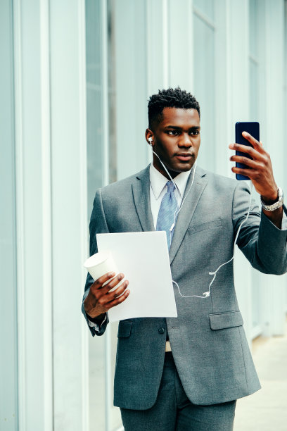 年轻的商人穿着西装在外面用智能手机图片下载