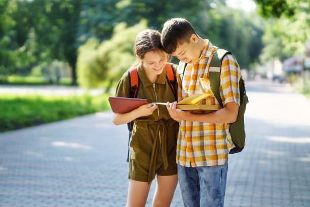 在城市公园的学生肖像，十几岁的学童一个男孩和一个女孩站在路上讨论功课，读书和交谈图片下载