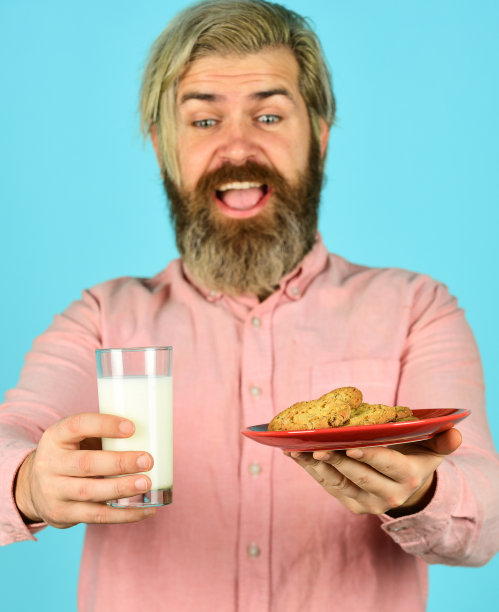 圣诞食品和饮料。圣诞饼干和牛奶。寒冷的圣诞节舒适概念。把饼干泡在牛奶里。快乐的农民吃着饼干甜点。胡子男人喝有用的牛奶配糕点图片下载