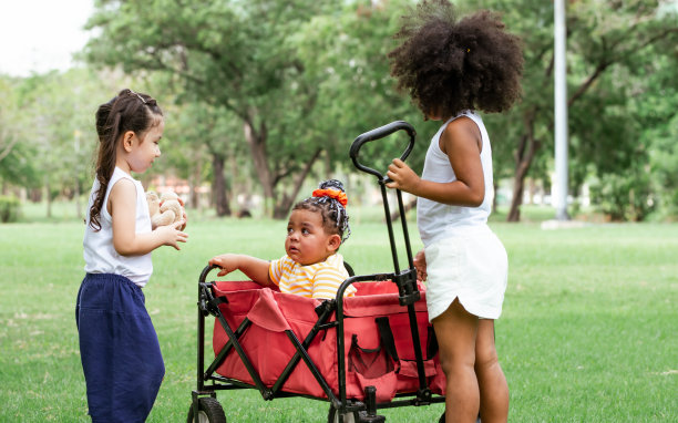 混合种族的可爱的小孩子拉和拖动一个红色的车在户外绿色公园玩。教育、多样性和团队合作理念。图片下载