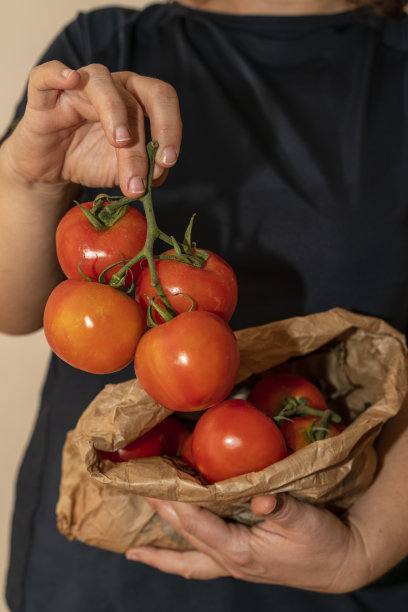 一个面目不明的女人拿着从回收纸袋里拿出来的有机红番茄图片下载