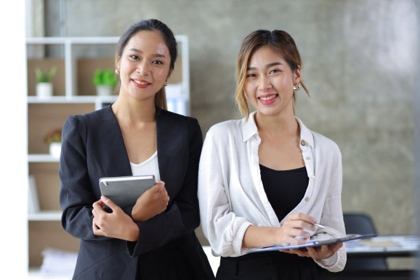 一位女商人和同事的肖像看着相机，在办公室快乐地微笑。图片下载