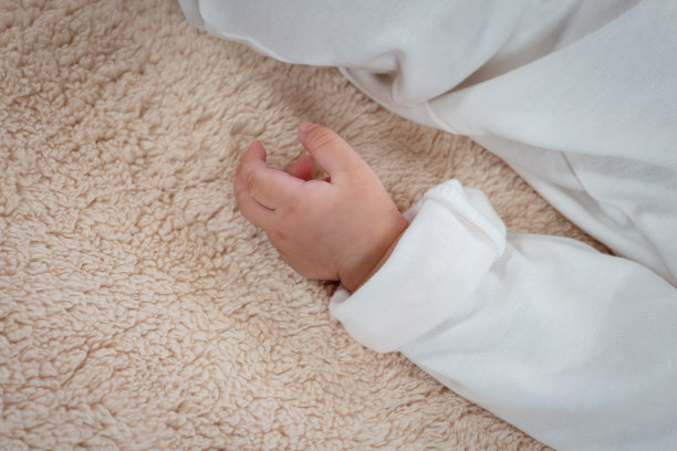 一个3个月大的亚洲新生儿的小手的特写照片，左手靠在一个小女孩的身体上。在卧室里睡在柔软的床上看起来很放松。图片下载
