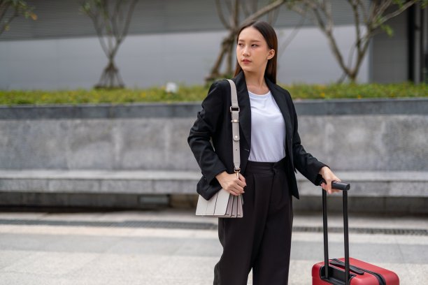 年轻酷看起来漂亮的亚洲女商人与她的红色行李微笑在她的办公楼外，而准备在去机场的路上图片下载