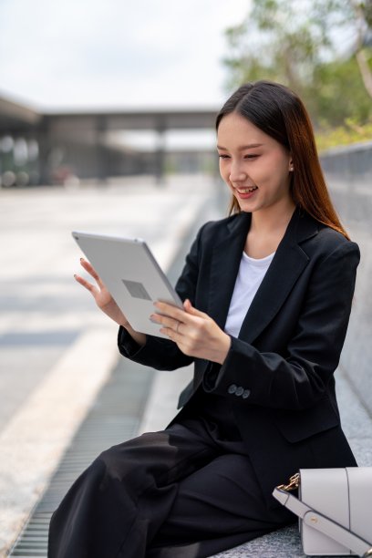 美丽年轻的亚洲女性办公室主管女士在她的办公大楼外，从她的平板电脑阅读最新的销售报告后开心地微笑图片下载