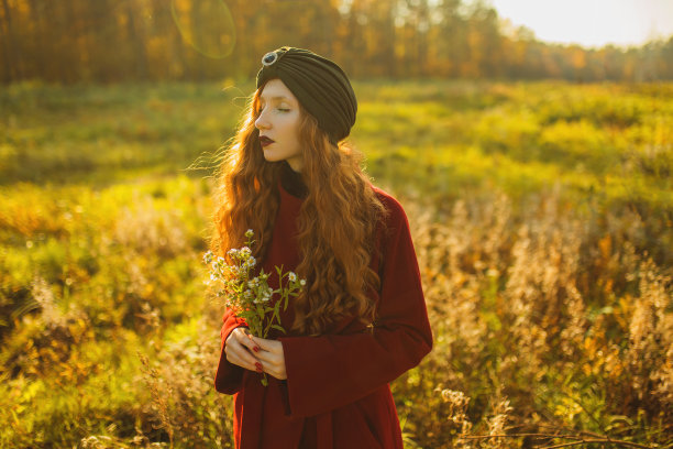 秋天的森林里，穿着大衣的红发卷发美丽女孩。戴头巾的漂亮女人在享受假期。感觉幸福。迷人的微笑。快乐的女士图片下载