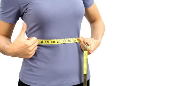 特写穿着运动服的女性手用卷尺测量腰围。健康营养与减肥理念。肖像在白色背景与演播室的光。图片下载