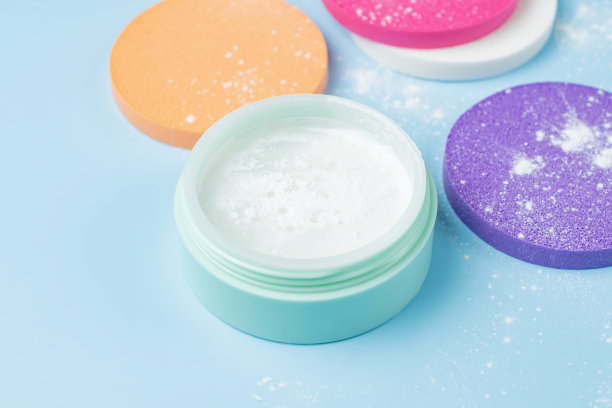 矿物松散的粉末在绿色的塑料容器和彩色海绵在前景。化妆的概念图片下载