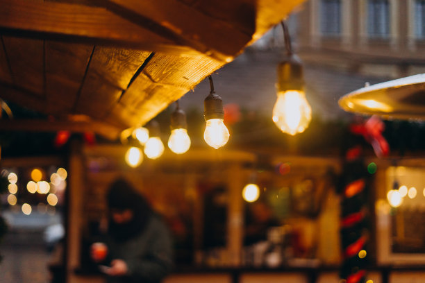 前景中的灯泡和模糊的背景。新年集市上木屋上的灯泡。欧洲圣诞市场背景上的一排花环。图片下载