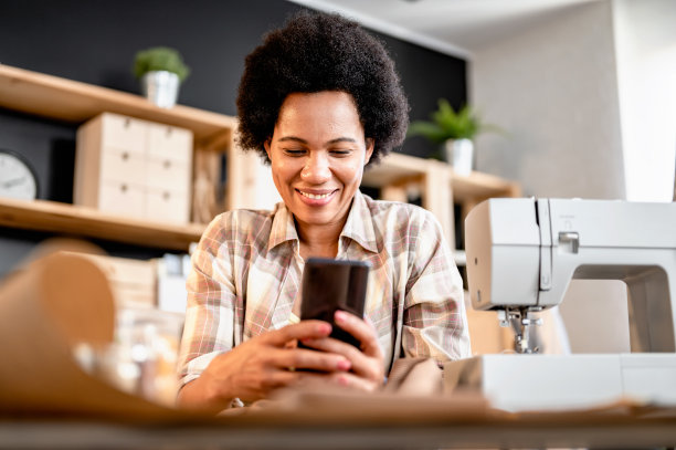 年轻的非洲裔女企业家在她的小作坊里用智能手机工作。面向企业家的在线银行应用程序图片下载