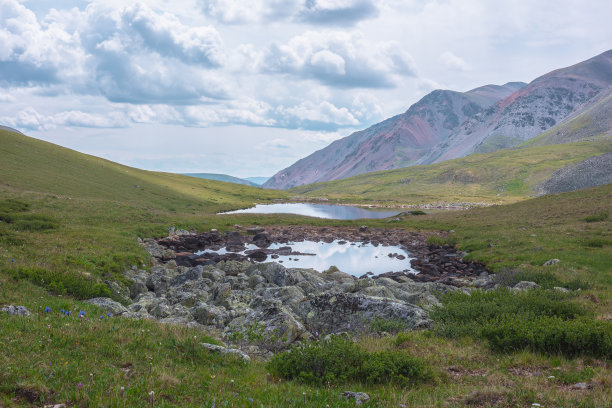 两山湖泊在山谷中，阴天下，绿山上。浮云倒映在水中的戏剧性风景，映照着青苔石间的小湖。图片下载