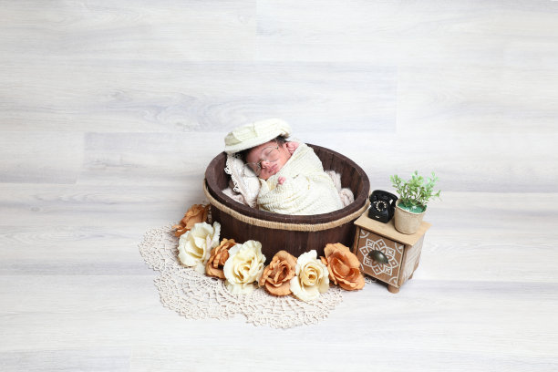 刚出生的可爱男孩盖着毛巾和帽子睡在木制圆碗装饰小道具和花图片下载