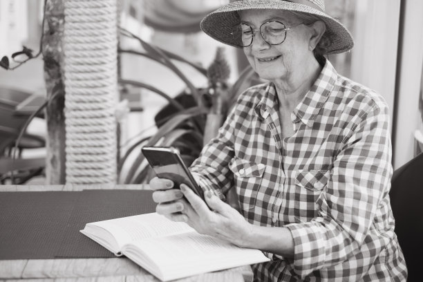 黑白肖像美丽的妇女与帽子坐在咖啡桌阅读信息电话，而白人女士享受自由时间和退休图片下载