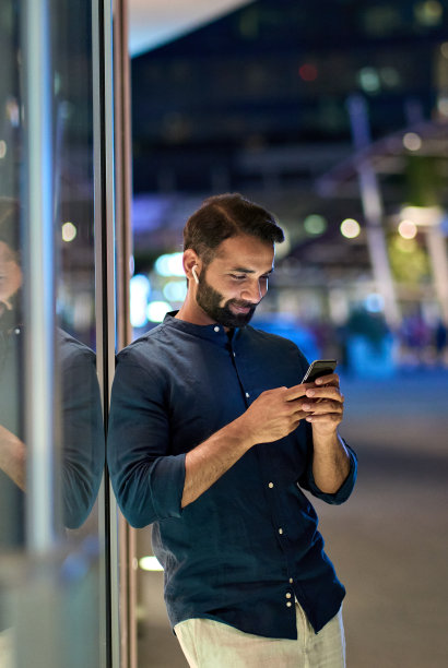 印度男人戴着耳机，晚上在户外拿着手机，竖版照片图片下载