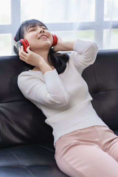 亚洲女性戴着耳机在家里的沙发上放松音乐图片下载