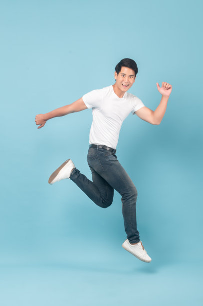 漂亮的亚洲人穿着白色t恤和牛仔裤在蓝色背景上跳跃图片下载