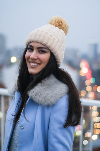 年轻的黑发女子与冬帽微笑肖像在城市图片下载