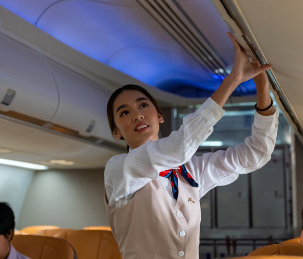 亚洲女性空姐在飞机起飞前关闭行李舱。图片下载