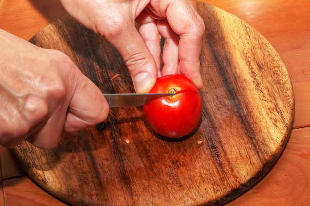 一位妇女正在用西红柿制作健康的新鲜果汁。女性用手在厨房的木板上切菜。健康生活方式的饮食观念。图片下载