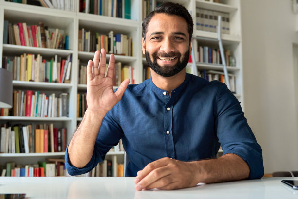 快乐的印度男老师通过视频通话挥手看着网络摄像头进行远程工作。图片下载