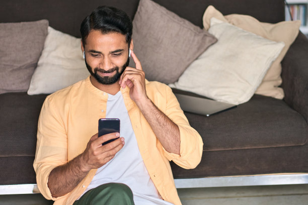 印度男子坐在家里的沙发上，用手机看视频图片下载