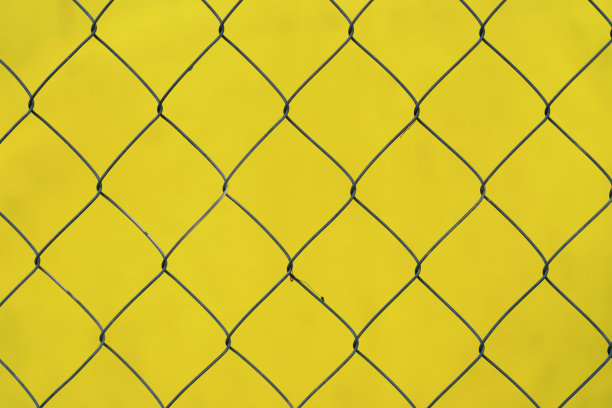 在黄色模糊的背景上由金属丝制成的铁链围栏的特写。图片下载
