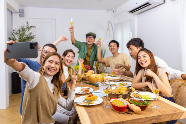 一群亚洲男女在家里一起吃饭，用手机自拍。图片下载