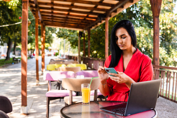 一位年轻的女商人正在一家花园咖啡馆里使用手机图片下载
