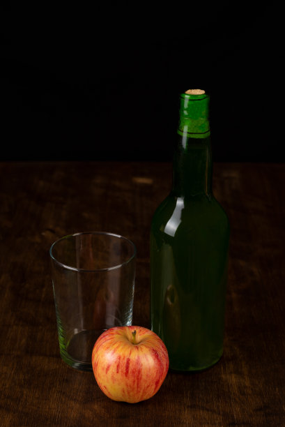 黑色的背景和木桌上，空杯子和苹果旁边放着一瓶苹果酒。图片下载