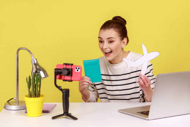 快乐的女博主展示护照和纸飞机的手机摄像头，并录制视频。图片下载