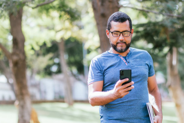英俊的商人在公园里用智能手机图片下载