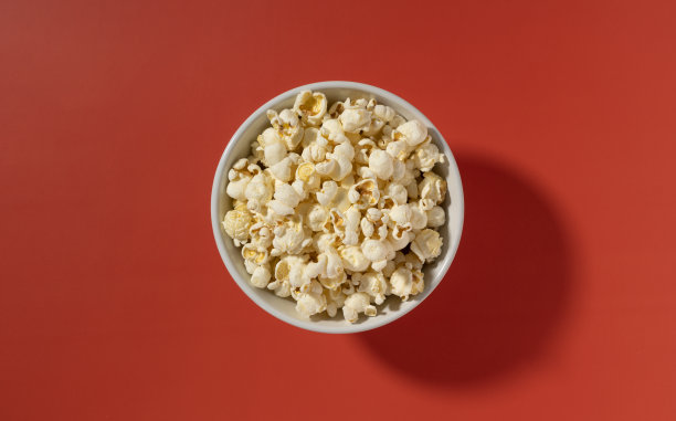 爆米花放在白色的碗里，放在红色的背景上。图片下载