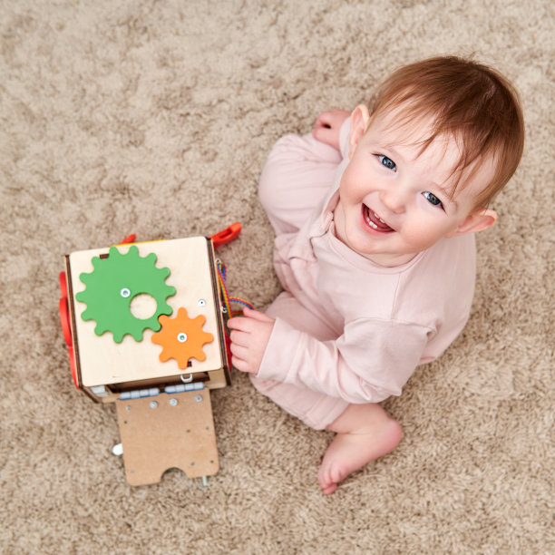 快乐蹒跚学步的小男孩正在婴儿室地板上玩一个纸板立方体。儿童益智玩具，木制游戏面板。一岁儿童一岁的孩子图片下载