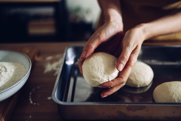 将面团放入金属托盘准备烘焙的手的特写图片下载
