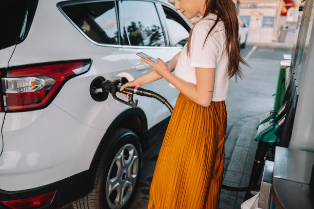 一名年轻女子在加油站加油时使用手机图片下载