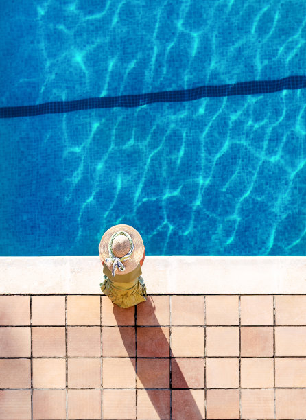 顶着一顶帽子的女人站在碧水的池边。垂直格式。放松和宁静的理念。图片下载