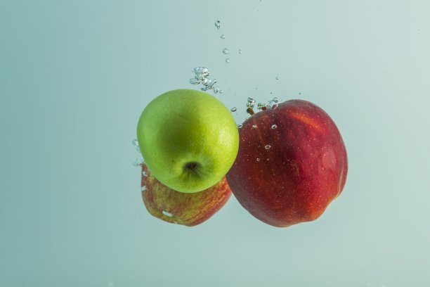 近距离观察红色和绿色的苹果落入水孤立在绿松石水的背景。图片下载