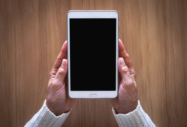 成熟女性双手捧着白色平板电脑，桌面背景上隔离着黑屏图片下载