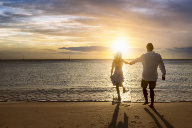 一对假日夫妇手牵着手享受金色日落时间的海滩图片下载